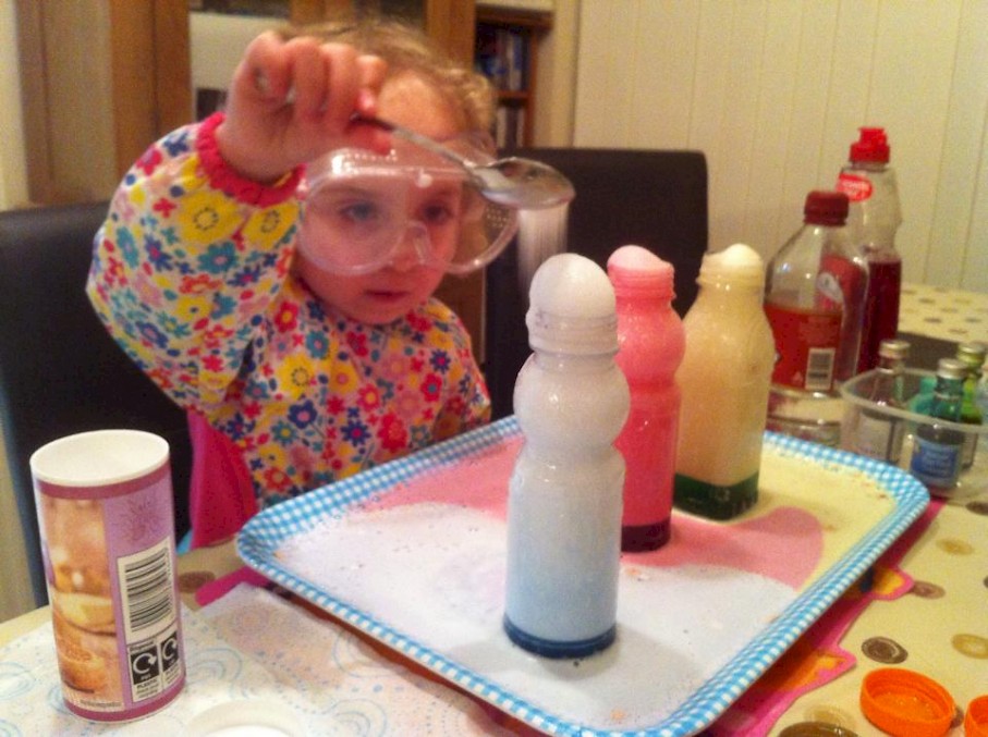 Baking soda being spooned into a bottle of blue foaming liquid