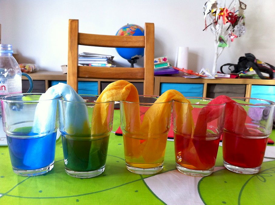 Coloured water flowing through kitchen towel between five glasses