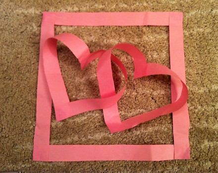 Two interlocking paper hearts within a paper square